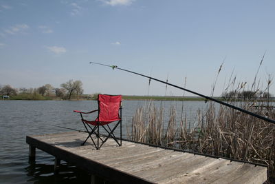 Fishing rod on pier over lake against sky