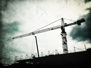 Low angle view of crane against cloudy sky