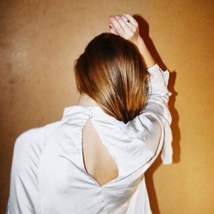 Rear view of woman standing against white wall at home