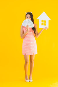 Full length portrait of woman standing against yellow background