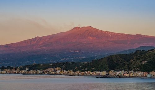 Scenic view of sea by mountains against sky during sunset