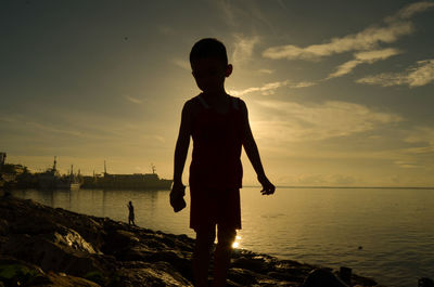 Silhouette boy standing on beach against sky during sunset