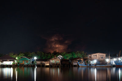 Illuminated buildings by lake against sky at night