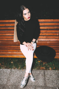 Full length of thoughtful young woman sitting on park bench at night