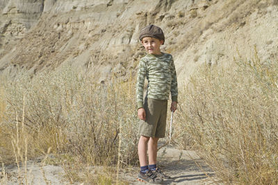 Boy standing on field against rock formation