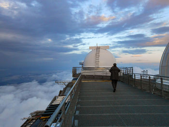 Rear view of man on railing and observatory against sky