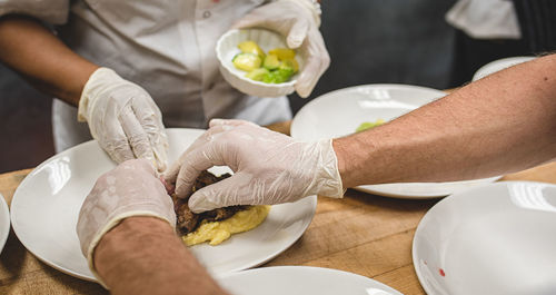 Cropped hands serving food in plates on table