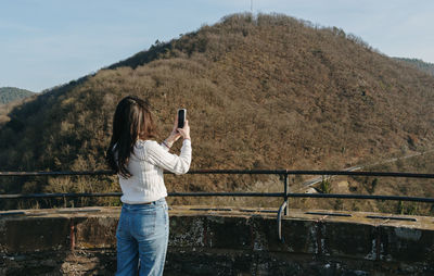 A girl takes a photo of the landscape on her smartphone from an observation deck.