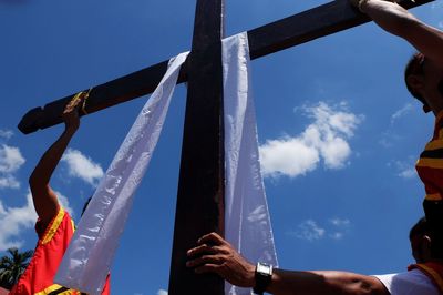 Cross with scarf amidst people against blue sky