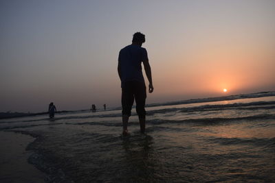 Silhouette man walking on beach against sky during sunset