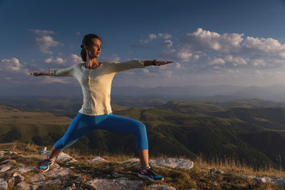 Yoga warrior pose of young caucasian woman practicing at sunset in the mountains in the grass. zen