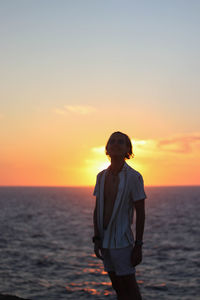 Funny backlit portrait of young man dressed in vintage clothes at sunset on mediterranean sea in 