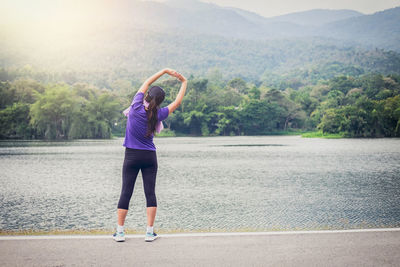 Full length of woman exercising at lakeshore