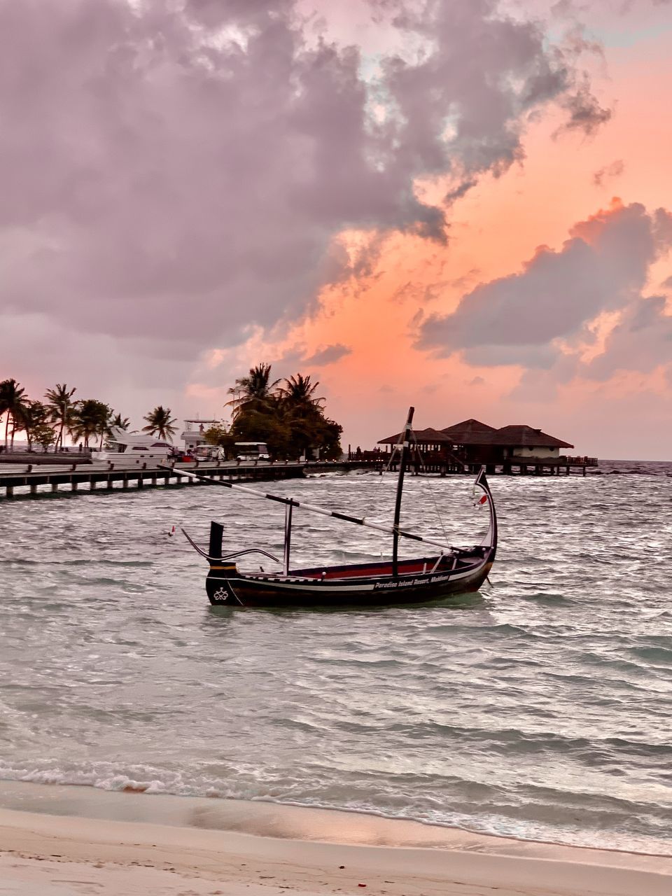 water, nautical vessel, sea, transportation, sky, sunset, mode of transportation, beach, land, shore, cloud, nature, travel, beauty in nature, vehicle, travel destinations, scenics - nature, long-tail boat, wave, boat, tropical climate, holiday, ocean, tourism, environment, vacation, trip, tranquility, coast, outdoors, architecture, sand, landscape, tree, palm tree, occupation, watercraft, tranquil scene, seascape, idyllic, activity, sun, tradition, no people, bay, motion, city