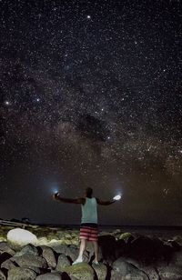 Rear view of man standing on rock at night