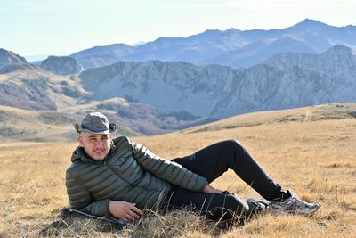 Man sitting on field by mountains