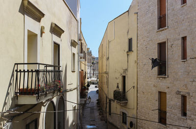 Rear view of man walking on alley amidst buildings in city