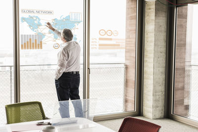 Businessman touching windowpane with world map and global network in office