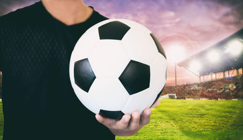 Midsection of man holding soccer ball on field