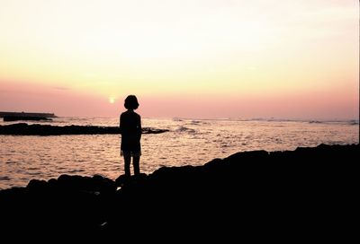 Silhouette man standing in front of sea during sunset