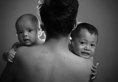 Rear view of shirtless father carrying son against gray background