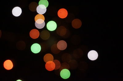 Defocused image of illuminated lights against sky at night