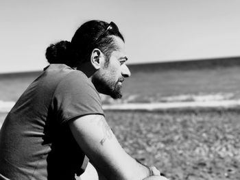 Side view of thoughtful mature man sitting at beach against clear sky