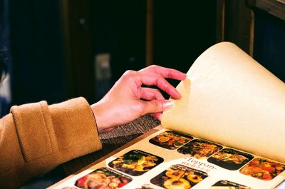 Cropped hand of woman holding menu at table in restaurant