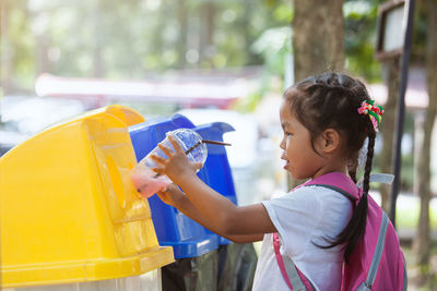 Side view of girl putting disposable glass in garbage can