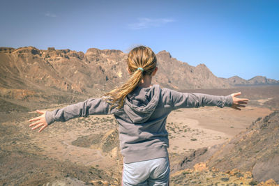 Rear view of girl with arms outstretched standing at desert