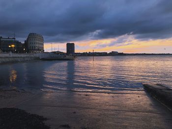 Scenic view of sea by buildings against sky at sunset