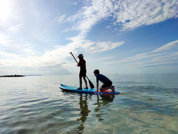 Siblings paddleboarding on sea against sky