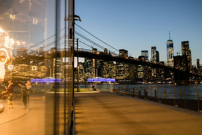 Illuminated bridge over river by buildings against sky in city