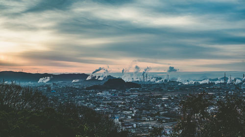 Cityscape and industry against sky during sunset