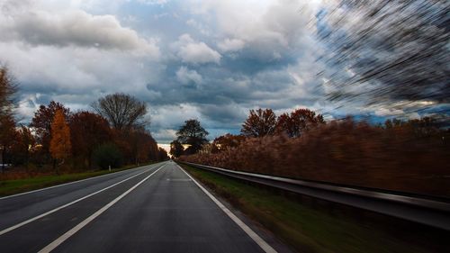 Road by trees against dramatic sky