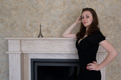 Portrait of young woman posing by eiffel tower replica on fireplace mantel at home