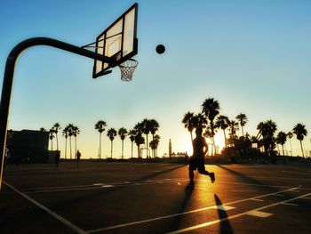 Silhouette man playing basketball on field against sky during sunset