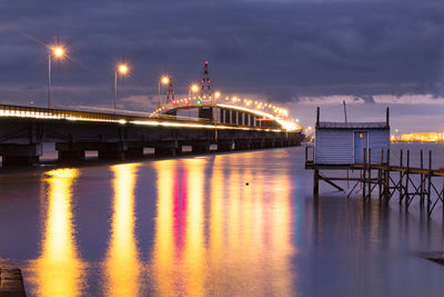 Illuminated pier over sea against sky at night