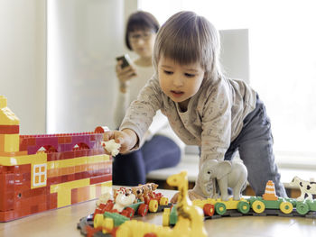 Toddler plays with toy blocks,his mother  babysitter texting in smartphone. kindergarten or nursery.