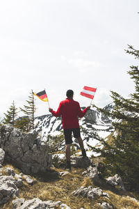 Rear view of mature man holding national flags while standing against snowcapped mountain