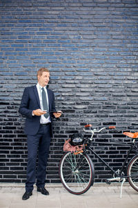 Full length of a man with bicycle standing against brick wall