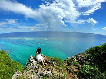 High angle view of woman sitting on rock over sea against sky