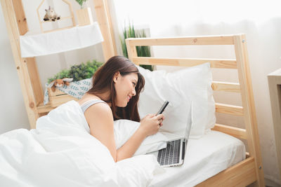 Young woman using mobile phone while sitting on bed