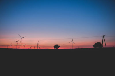 Silhouette wind turbines on field against sky during sunset