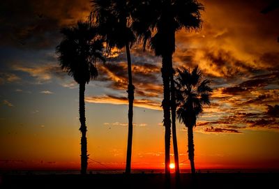 Silhouette palm trees by sea against romantic sky at sunset