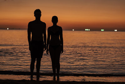 Silhouette couple standing on beach against sky during sunset