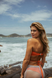 Portrait of young woman standing at beach against sky