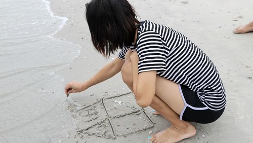 Low section of girl standing on wet sand at beach