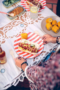 Midsection of young woman holding hot dog in plate on table