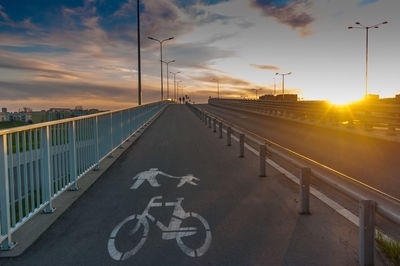 Road leading towards bridge against sky during sunset